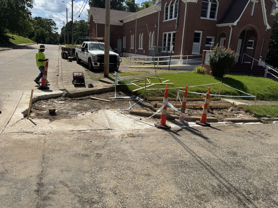 Silverback crew removing and reforming curb, gutter, and street-side sidewalk in front of a brick church with traffic cones and wood forms in place