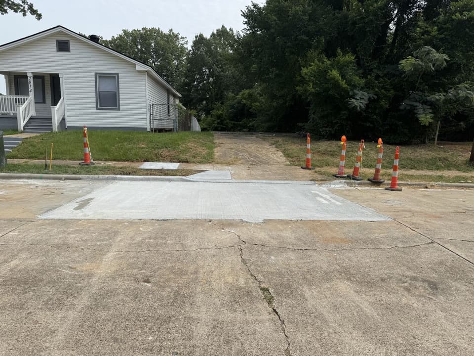 Newly poured concrete driveway approach at a Northwest Louisiana residence, finished flush to the existing street with traffic cones staged